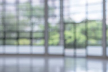 Arka plan bulanık. Boş ofis lobisine, giriş kapılarına ve cam perde duvarına bakıyor. 