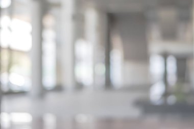 Arka plan bulanık. Boş ofis lobisine, giriş kapılarına ve cam perde duvarına bakıyor. 