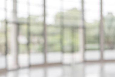 Arka plan bulanık. Boş ofis lobisine, giriş kapılarına ve cam perde duvarına bakıyor. 