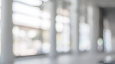 Arka plan bulanık. Boş ofis lobisine, giriş kapılarına ve cam perde duvarına bakıyor. 