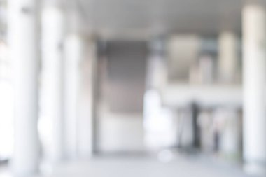 Arka plan bulanık. Boş ofis lobisine, giriş kapılarına ve cam perde duvarına bakıyor. 