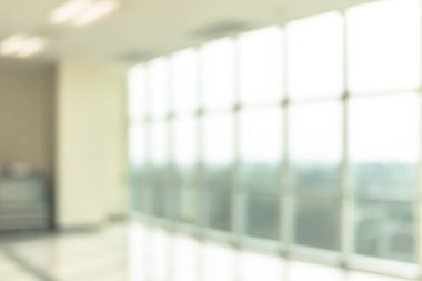 Arka plan bulanık. Boş ofis lobisine, giriş kapılarına ve cam perde duvarına bakıyor. 