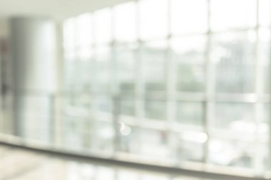 Arka plan bulanık. Boş ofis lobisine, giriş kapılarına ve cam perde duvarına bakıyor. 