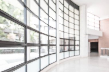 Arka plan bulanık. Boş ofis lobisine, giriş kapılarına ve cam perde duvarına bakıyor. 