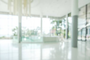 Arka plan bulanık. Boş ofis lobisine, giriş kapılarına ve cam perde duvarına bakıyor. 