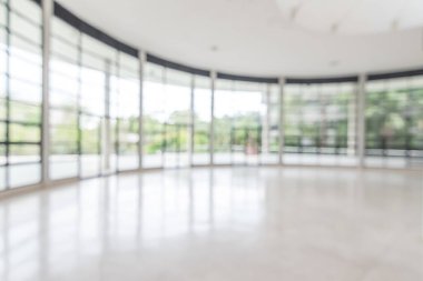 Arka plan bulanık. Boş ofis lobisine, giriş kapılarına ve cam perde duvarına bakıyor. 