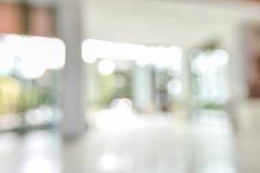 Arka plan bulanık. Boş ofis lobisine, giriş kapılarına ve cam perde duvarına bakıyor. 