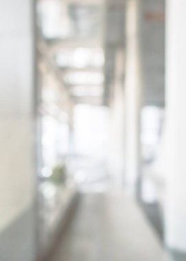 Arka plan bulanık. Boş ofis lobisine, giriş kapılarına ve cam perde duvarına bakıyor. 