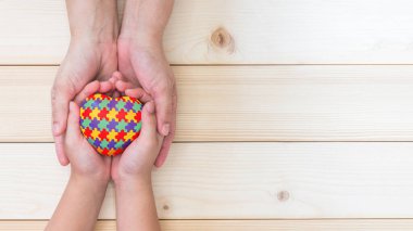 Dünya Otizm Farkındalık Günü konsepti. Yapboz ya da yapboz desenli. Otistik çocuk elleriyle bakıcı aile tarafından destekleniyor. 