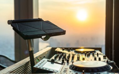 DJ Disk Jokey çatı partisi, lüks restoran yemeği ve gece kulübü ses eğlencesi için kontrol edicisi. Akşam günbatımı şehir manzarası arka planında dijital tablet müzik dosyasıyla birlikte.
