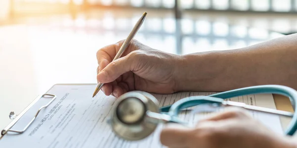 Medical doctor writing on patient personal health care record discharge form, or prescription paperwork in hospital office, clinic center for healthcare and life insurance concept