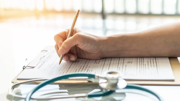 Medical doctor writing on patient personal health care record discharge form, or prescription paperwork in hospital office, clinic center for healthcare and life insurance concept