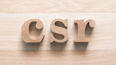 CSR Kurumsal Sosyal Sorumluluk, şirket vizyonu kısaltması ve doğal beyaz ahşap arka planda geri dönüşüm tahtasından yapılmış kısaltma harfleriyle sorumlu yönetim kavramı.
