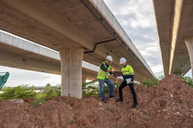 İki inşaat işçisi proje detaylarını otoyol gösteriminde takım çalışması ve sanayi dinamiği altında tartıştı.