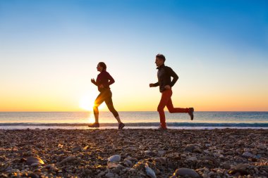 Sportif çift sabah koşu deniz plajda güneş doğarken yapıyor