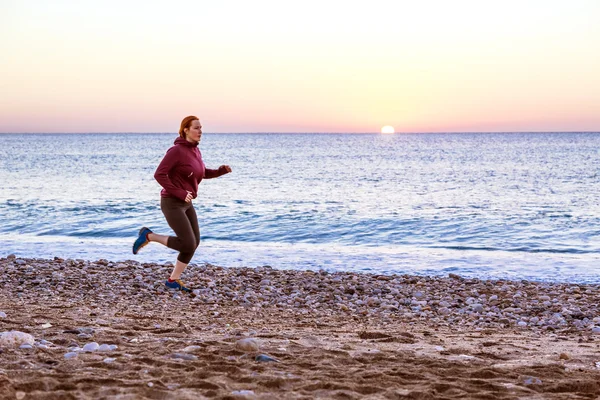 Junge Frau joggt am Strand entlang der Brandung bei Sonnenaufgang — Stockfoto