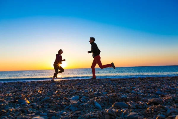 Silhouetten von Mann und Frau, die bei Sonnenaufgang am Strand entlang joggen — Stockfoto