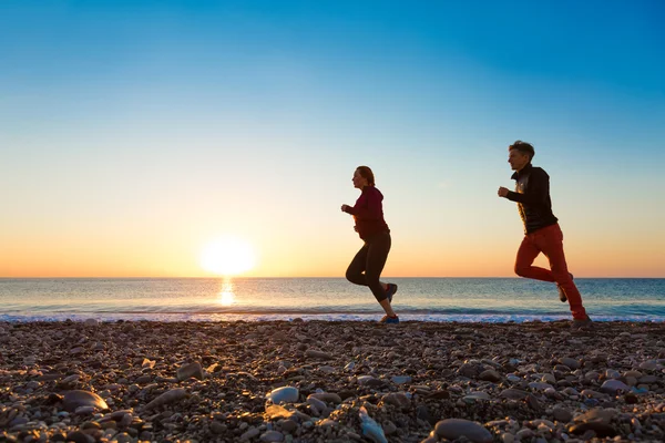 Sportif çift sabah koşu deniz plajda güneş doğarken yapıyor — Stok fotoğraf