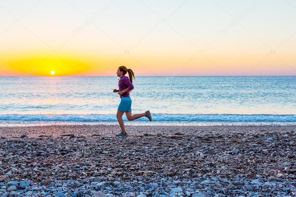 Sporty Girl jogging on Beach along Sea Surf at Sunrise