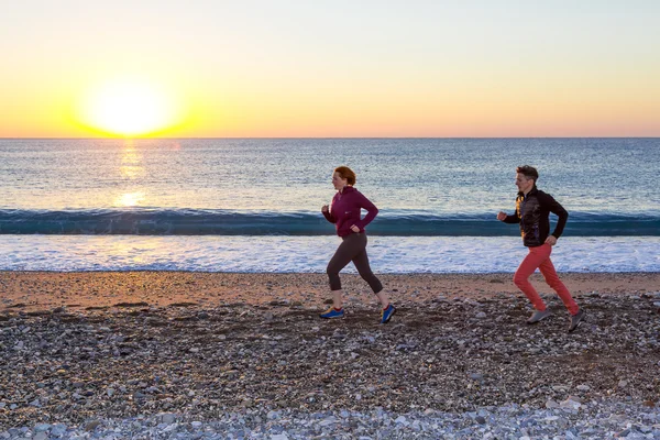 Sportliches Paar beim morgendlichen Joggen am Strand bei Sonnenaufgang — Stockfoto