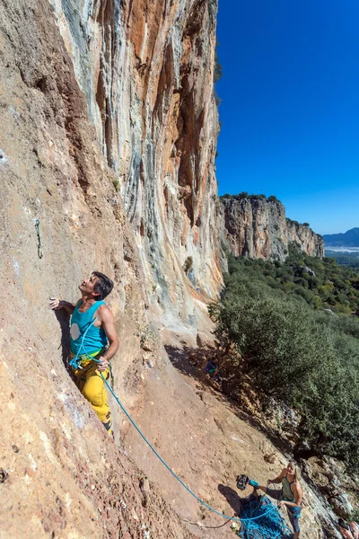 Mogna manlig extrema klättrare flyttar upp på belay partner — Stockfoto