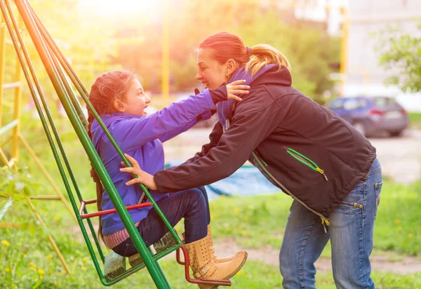 Joven madre montando pequeña hija en el balancín en Spring Park — Foto de Stock