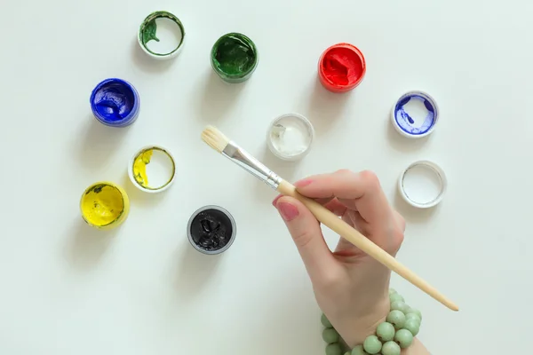 Mano del artista sosteniendo el pincel y el color Pinturas sobre mesa blanca — Foto de Stock