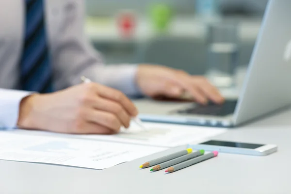 Geschäftsmann arbeitet an Laptop und gedruckten Charts — Stockfoto