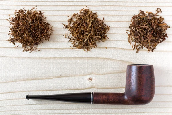 Drie verschillende soorten tabak en pijp op houten achtergrond — Stockfoto