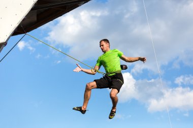 Mavi gökyüzünde uçan erkek dağcı tırmanma duvarının dökülmesi