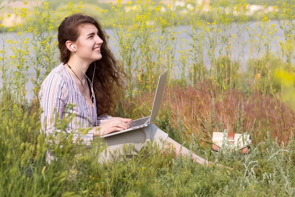 Счастливая молодая женщина с компьютером на лугу травы — стоковое фото