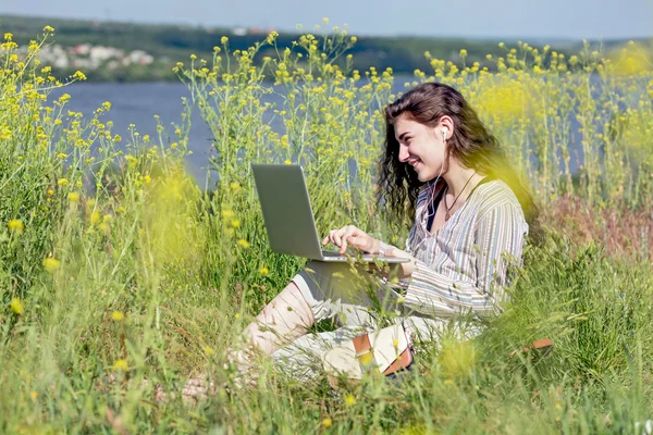 Счастливая молодая женщина с компьютером на лугу травы — стоковое фото