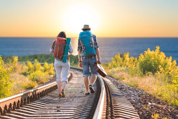 Homem e mulher com mochilas e guitarra caminhando em direção ao mar — Fotografia de Stock