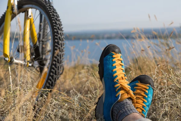 Человек в яркой спортивной обуви отдыхает на траве вдоль велосипеда — стоковое фото