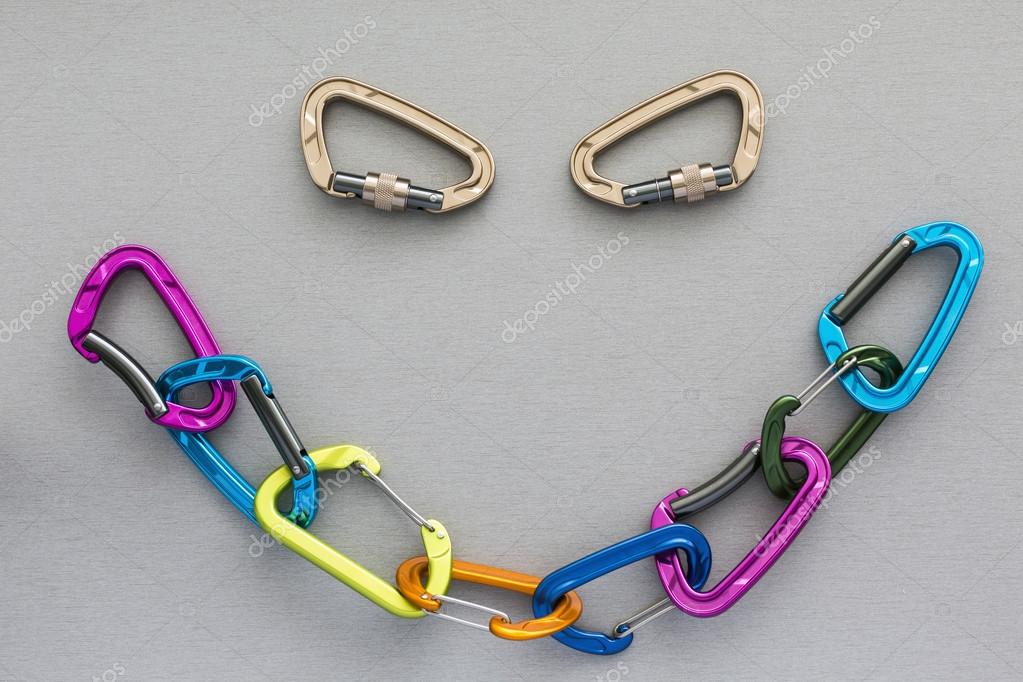 Many colored extreme climbing devises linked in the chain and forming the smiley shape. Two separate devises form an eyes of face