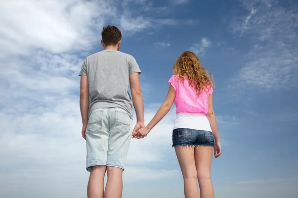 Casal jovem fica na frente do céu azul nublado — Fotografia de Stock