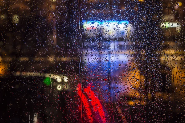 Raindrops on the window with urban night lights — Stock Photo, Image