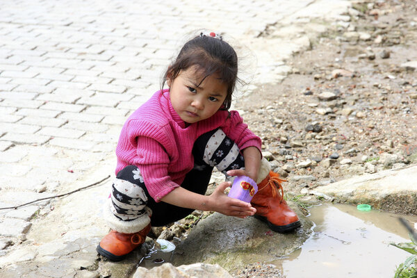 Little baby girl of Chinese hani minority plays in puddle on road