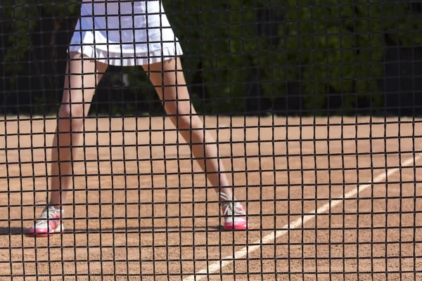 Slim piernas de mujer atleta de tenis detrás de la barrera de red de pesca —  Fotos de Stock