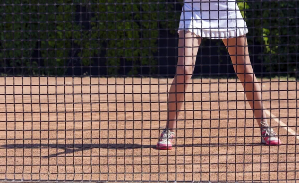 Slim piernas de mujer atleta de tenis detrás de la barrera de red de pesca —  Fotos de Stock