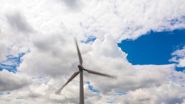 Wind energy generator with rotating blades on massive dramatic cloud blue sky daylight outdoor