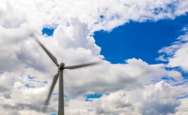 Wind energy generator with rotating blades on massive dramatic cloud blue sky daylight outdoor