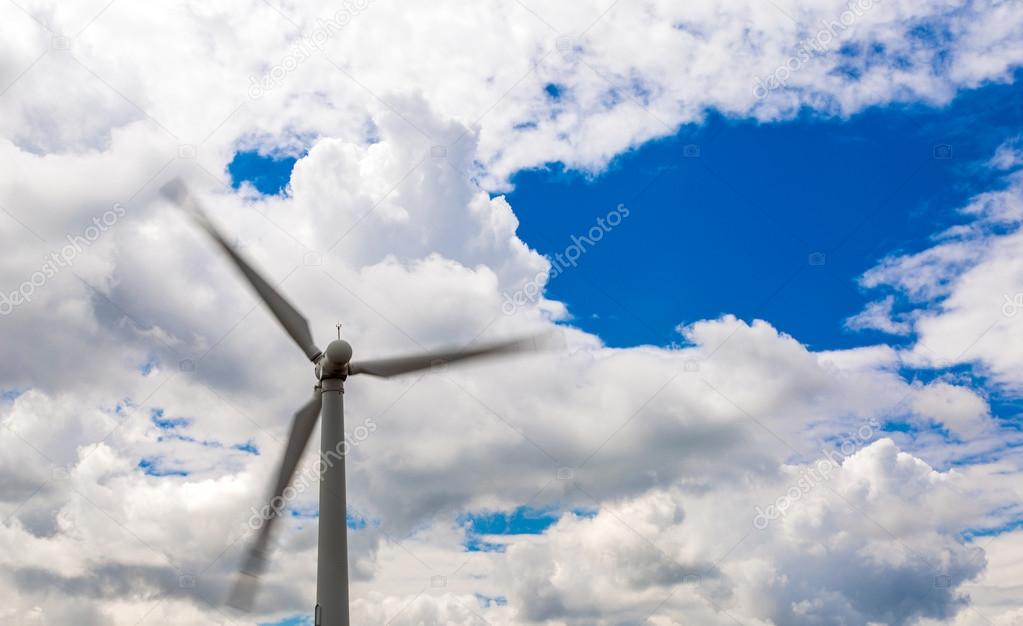 Wind energy generator with rotating blades on massive dramatic cloud blue sky daylight outdoor