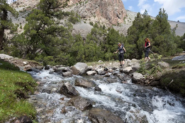 Two hikers crossing fast flowing river — Stock Photo, Image