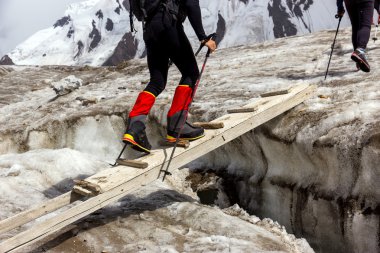 People Crossing Glacier Crevasse on Wood Shaky Footbridge clipart