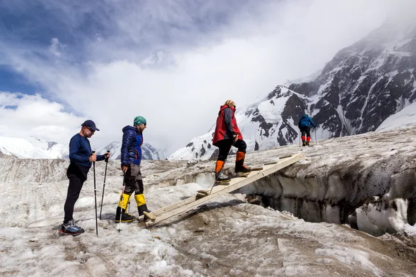 Människor korsar Glacier spricka på trä skakig gångbro — Stockfoto