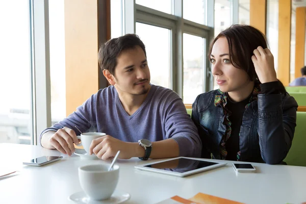 Junges Paar am weißen Kaffeetisch mit Kaffeebechern und Gadgets — Stockfoto