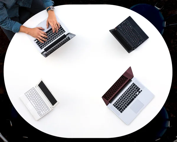 Vista superior del escritorio redondeado con cuatro computadoras portátiles y manos masculinas escribiendo en el teclado —  Fotos de Stock