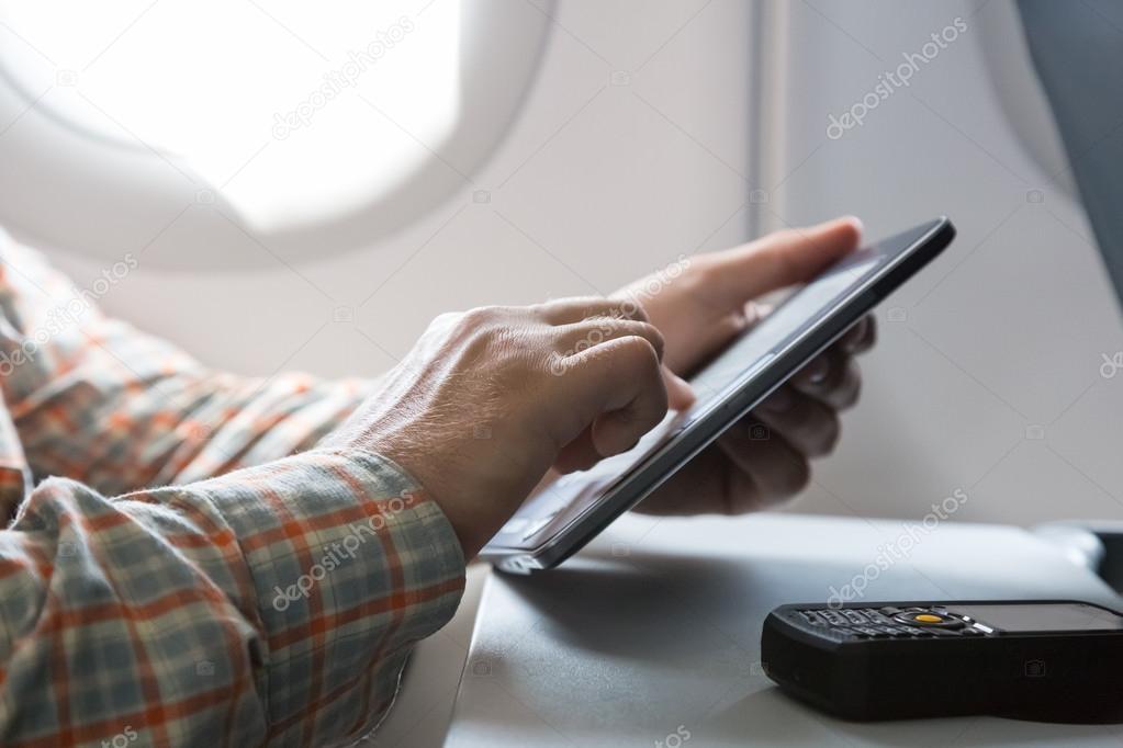 Hands of man browsing gadget in aircraft