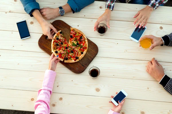 Handen van mensen aan hout Cafe Pizza tafel met dranken eten en elektronische Gadgets — Stockfoto